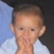 Image depicts Daniel Corby - a young Caucasian boy with short blonde hair. He has both hands in front of his mouth and seems to be happily sucking on his fingers.