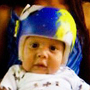 Image depicts Noe Medina Jr. - a Hispanic baby boy wearing a blue and yellow helmet looking intensely into the camera.