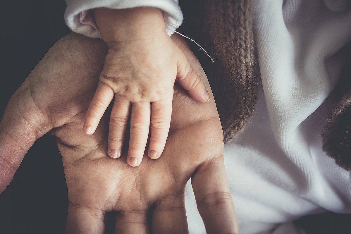 Nahaufnahme der Hand eines Babies, die in der Hand eines Erwachsenen ruht.