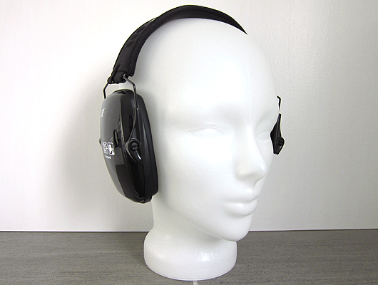 White background, grey floor, white glass head wearing slim black ear defenders.