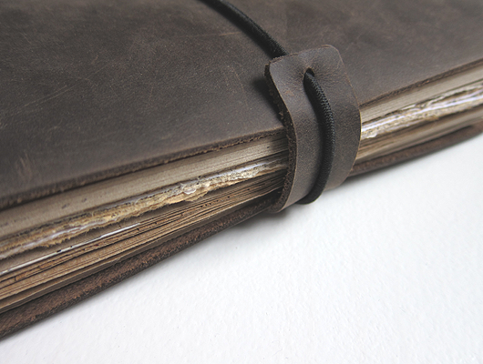 Handmade planner with dark brown leather cover and a variety of paper inserts in shades of brown.