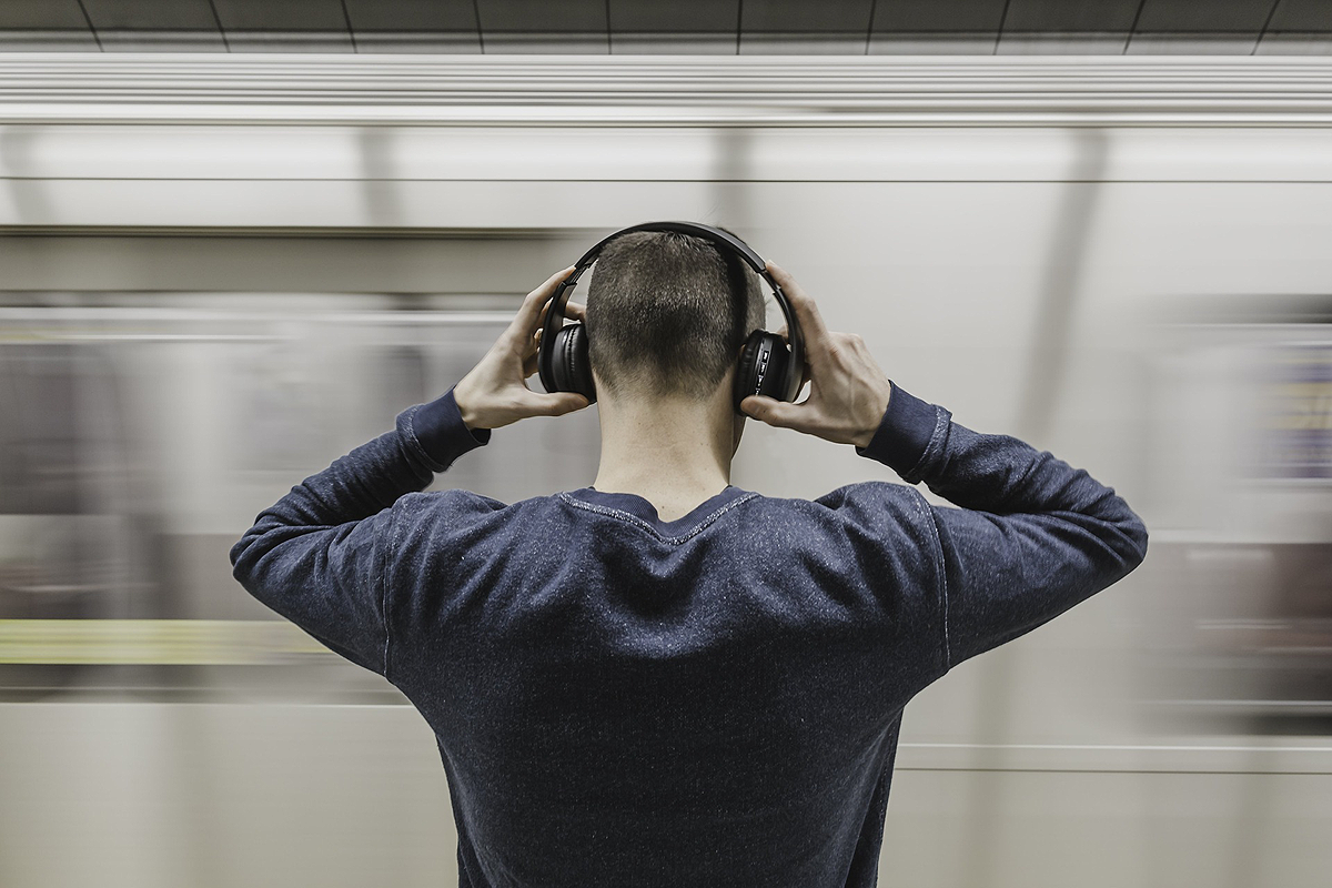 Person standing with their back to the camera. They are putting large over ear headphones on, their hands are still on them.