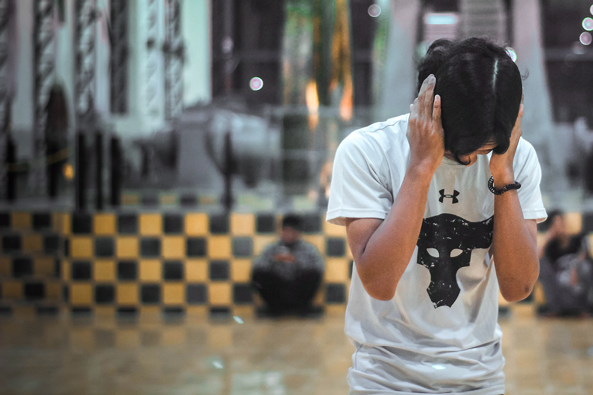 Person of color covering their ears infront of a busy public area background.