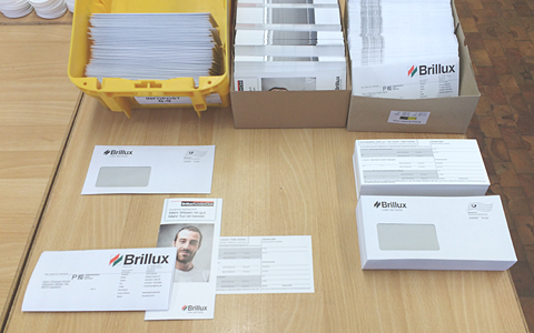 A desk with three boxes filled with finished mail, flyers, and pre-folded letters. In front of the boxes the materials are layed out how they go into the envelopes.