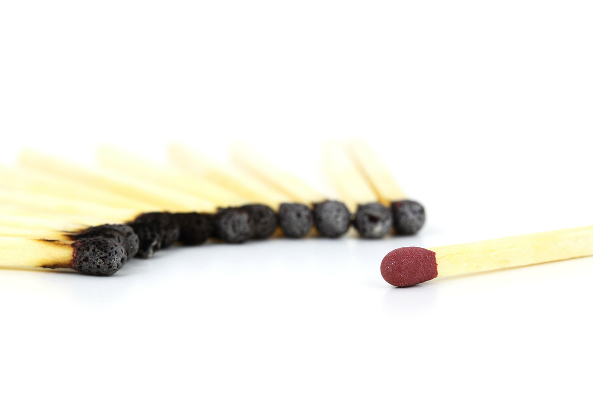A half circle of burnt matches on the left and a single unburnt match on the right, infront of a white background.