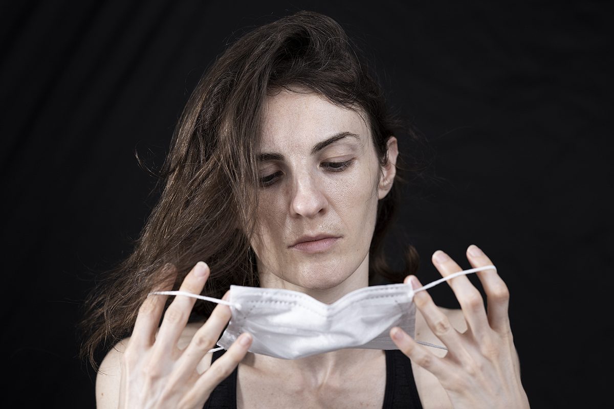 Light skinned person with long brown hair, looking down onto a face mask they are holding in their hands.