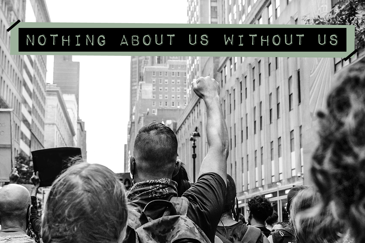 Black and white image of a protesting crowd marching in the streets. Centered is a protestor raising their fist into the air. The activism slogan "Nothing about us without us" is written in bold, all capital, label style font at the top.