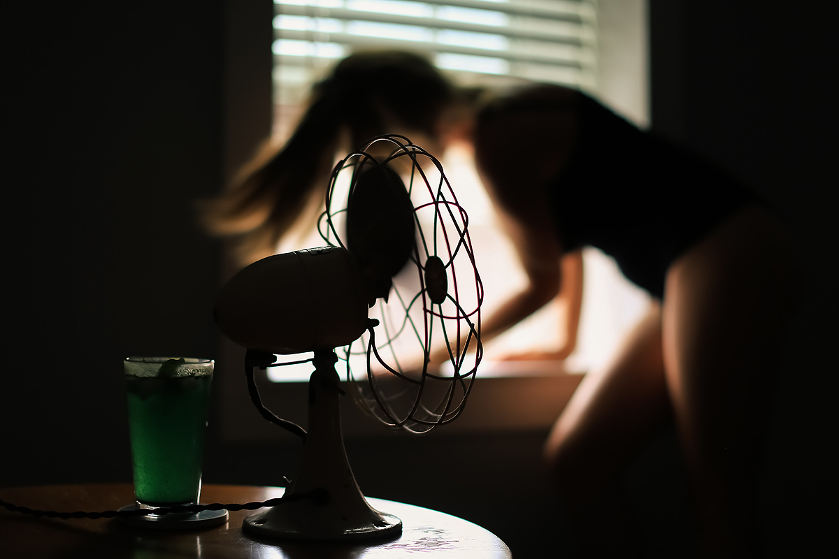 Person with long flowing hair blurry in the background in front of a window. A fan is blowing in the foreground.